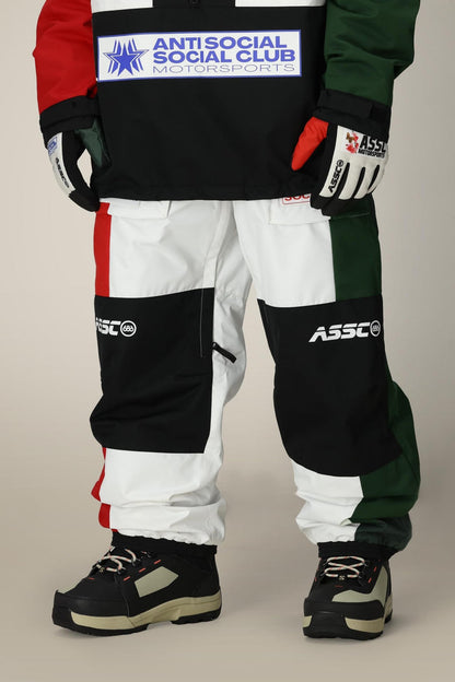 A person wearing 686 Mens ASSC F1 Shell Pant in color-blocked black, white, red, and green with ASSC logos, paired with black and beige boots, gloves also featuring ASSC logos, and an Anti Social Social Club Motorsports jacket.