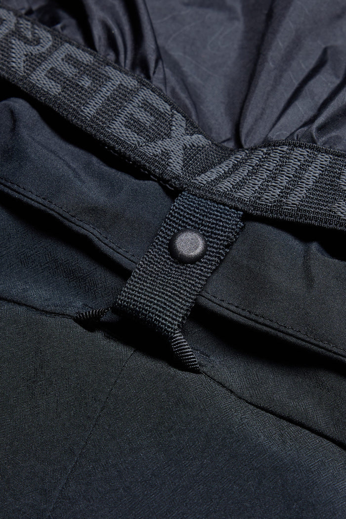 Close-up of the 686 Men's Deconstructed™ Denim Pant in black, showing its waterproof insulated design with a snap button waistband and visible "GORE-TEX" branding, emphasizing the textured fabric and precise construction by 686.