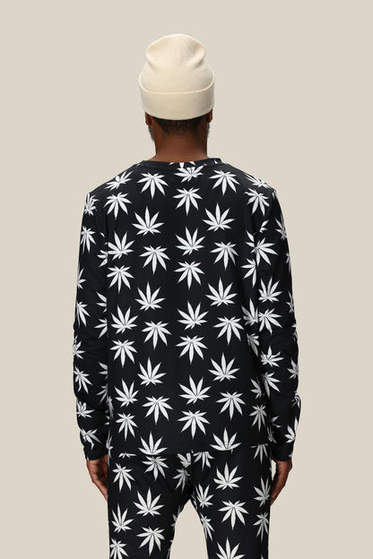 A person wearing the 686 Men's HUF Plantlife Base Layer LS Top stands facing away from the camera against a plain beige background.