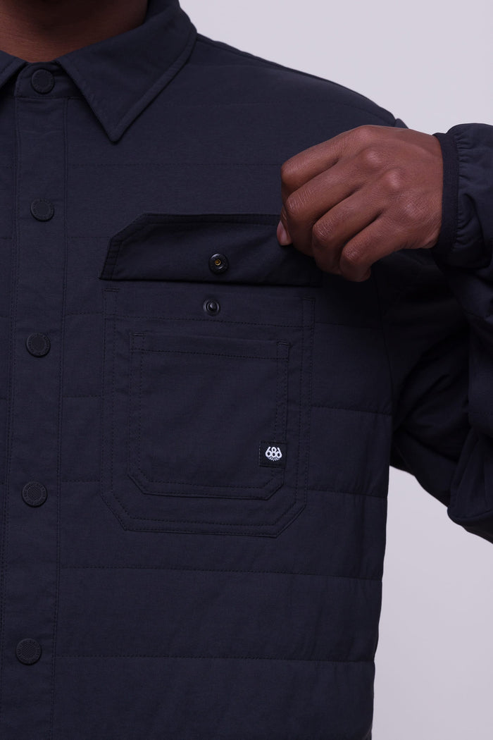 A person wearing the 686 Men's Thermaldry™ Snap-Up Shirt unbuttons the chest pocket flap. The shirt by 686 features a pointed collar and visible stitching on the pocket.
