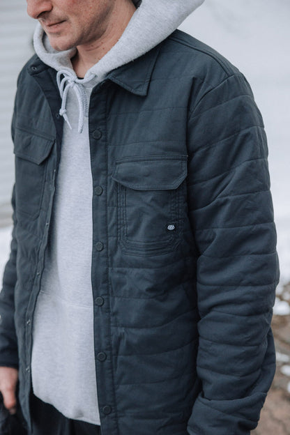 A person wearing the 686 Men's Thermaldry™ Snap-Up Shirt stands outdoors. Only the lower half of their face and upper body, layered beneath a grey hoodie, are visible in this cropped image.