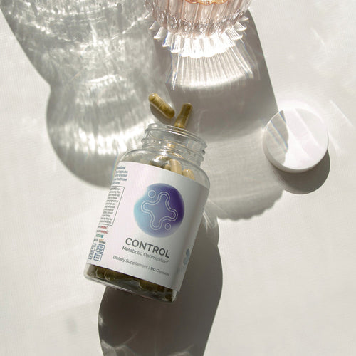 InfiniWell Control Metabolic Optimization dietary supplement bottle with open lid and capsules on a sunlit white surface.