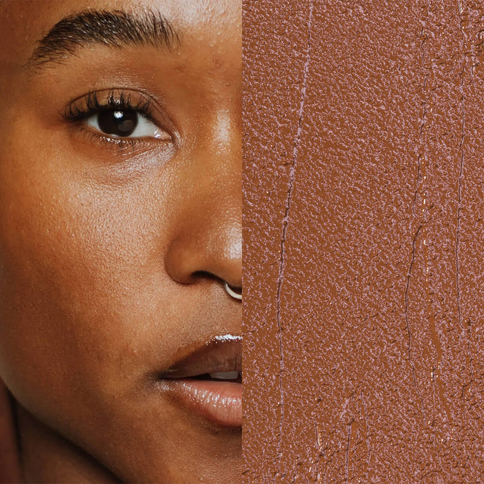 Model next to swatch of Elate Beauty Creme Concealer in the shade 'CW6', for medium deep warm skin tones. A two-in-one concealer and illuminator formulated with evening primrose oil, designed to heal and conceal blemishes.