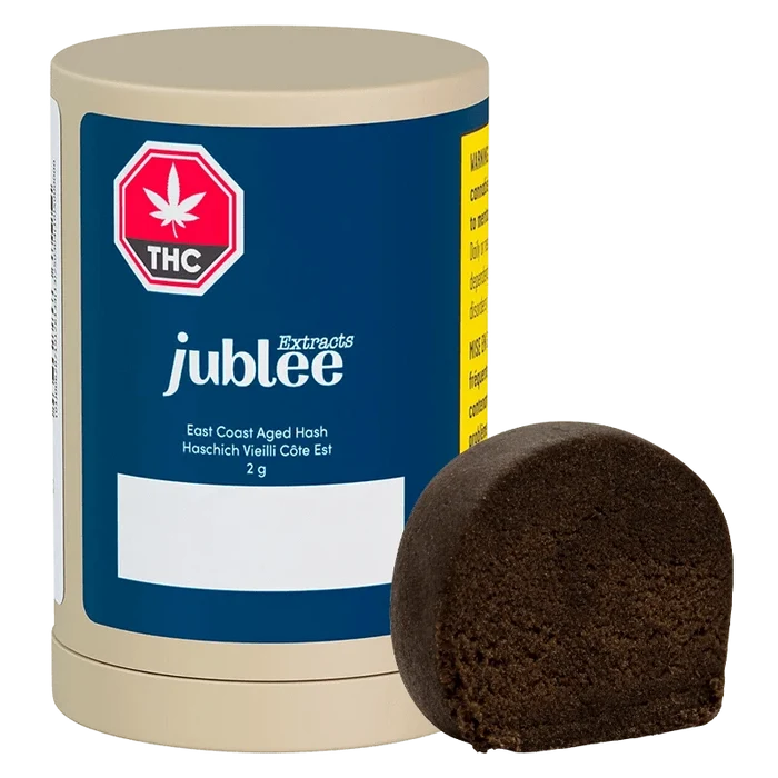 Front three-quarter view of a Jubilee Extracts East Coast Aged Hash 2 g cylinder with its dark brown half-disc of hash placed beside it.
