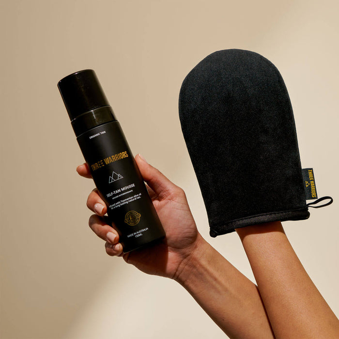 Hand holding a black spray can and black oven mitt against a beige background.