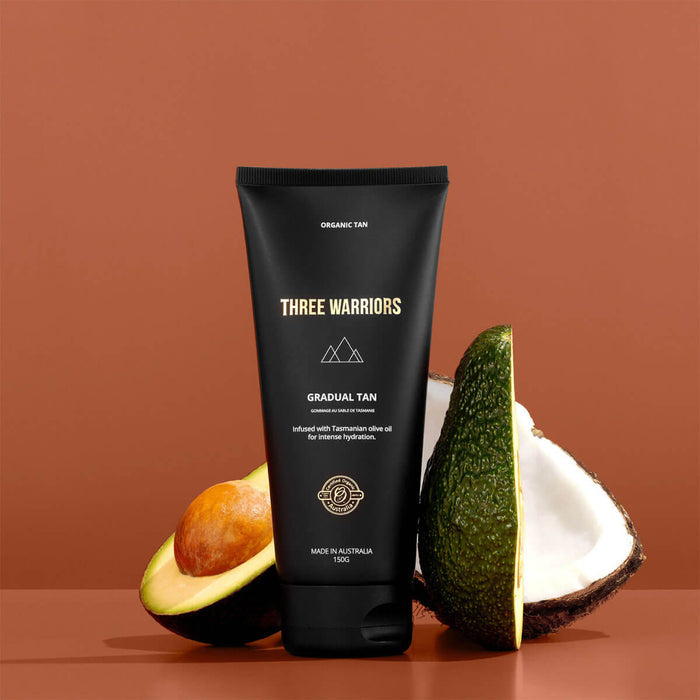 'Three Warriors gradual tan' product with avocado and coconut on a brown background.