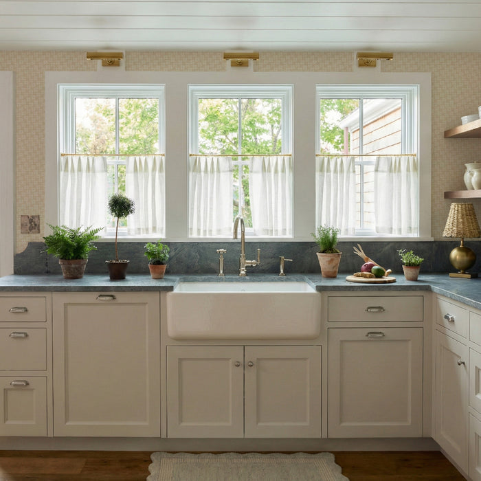 Bright kitchen with Gwen Sand wallpaper in subtle pattern, white cabinetry, marble countertop, and café curtains on windows.