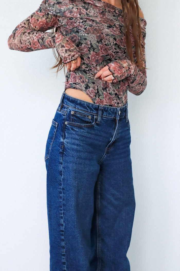 Person wearing a floral long-sleeve top and blue jeans against a white background