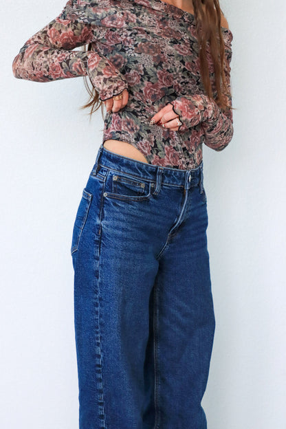 Person wearing a floral long-sleeve top and blue jeans against a white background