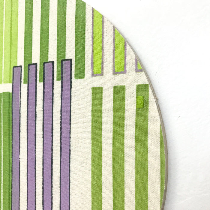 Line Study 1 by Molly Koehn features vertical stripes in varying shades of green and lavender on raw silk. The geometric composition shows parallel lines arranged in a rhythmic pattern against an off-white background, mounted on a circular birch panel. The embroidered texture adds depth to the minimalist design.