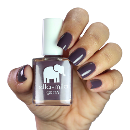 Night In dark purple nail polish on a medium skin tone, hand holding the bottle