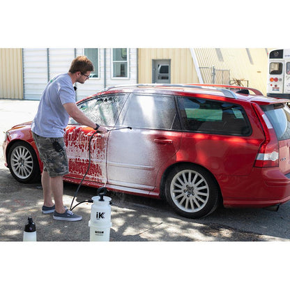 A person using a large IK Sprayer to spray foam onto a red vehicle.