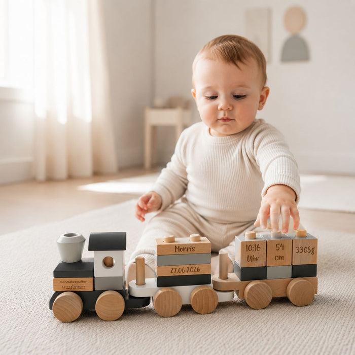 Baby hinter personalisiertem Holzzug zur Geburt in Grau und Natur mit Name und Geburtsdaten
