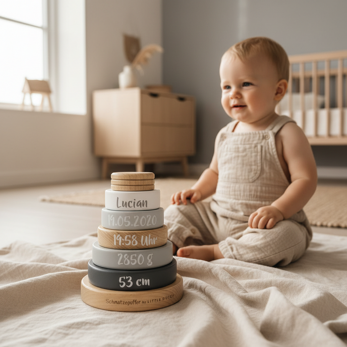 Baby neben grauem Holz-Stapelturm mit Name und Geburtsdaten als Erinnerung zur Geburt