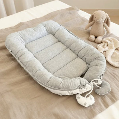 Wendbares tiSsi Babynest Grau/Weiß auf einem Bett – Produktansicht
