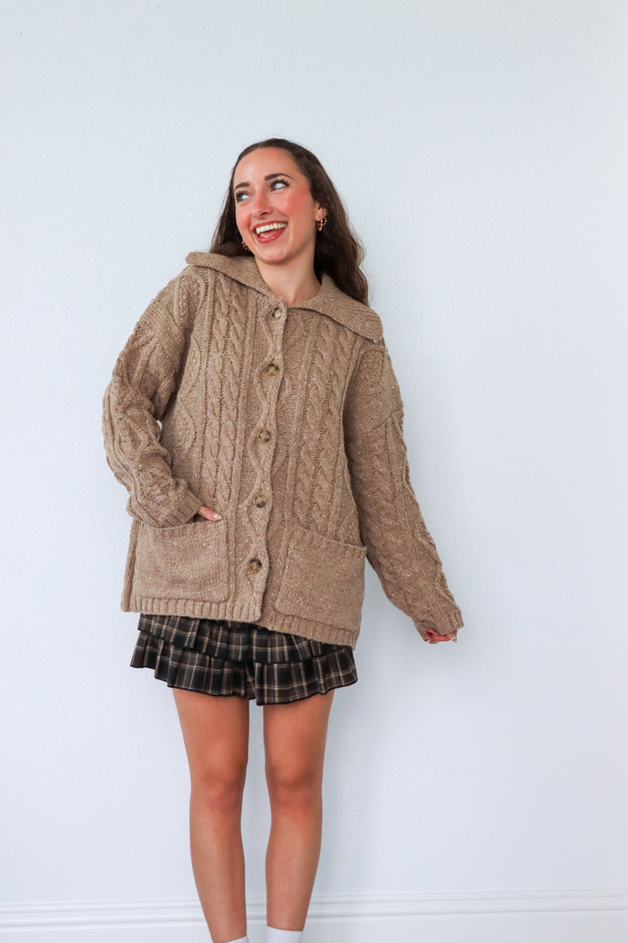 Woman wearing a brown cable knit cardigan against a white background