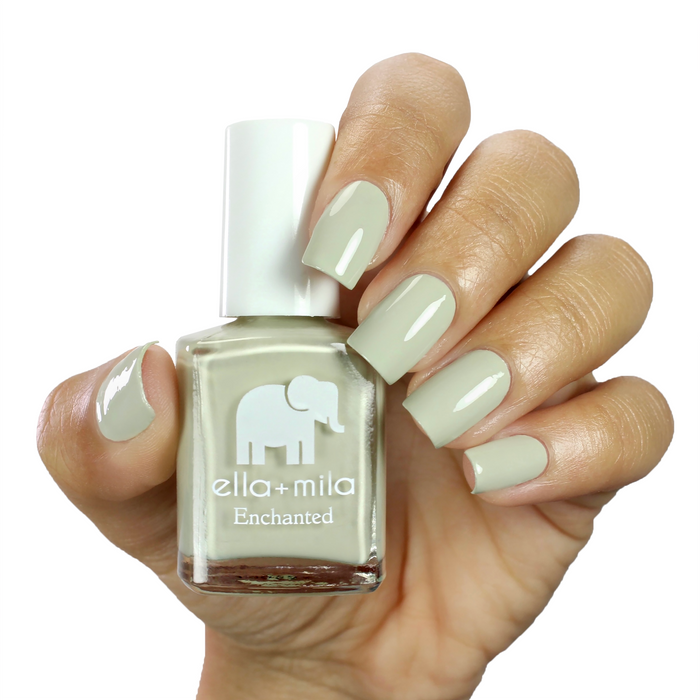 Sacred Sage dusty sage green nail polish on a medium skin tone, hand holding the bottle