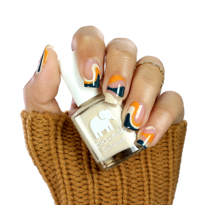 Secret Garden creamy nude nail polish with orange and black abstract accent nails, holding the bottle