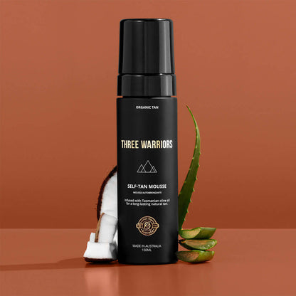 Three Warriors self-tan mousse bottle with aloe vera leaves on a brown background.
