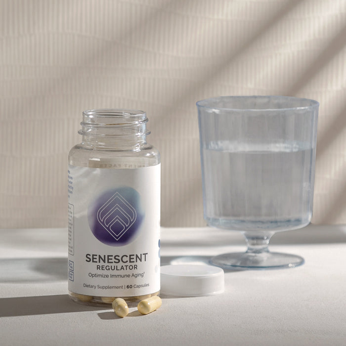 InfiniWell Senescent Regulator dietary supplement bottle with open lid, capsules, and glass of water on a neutral surface.