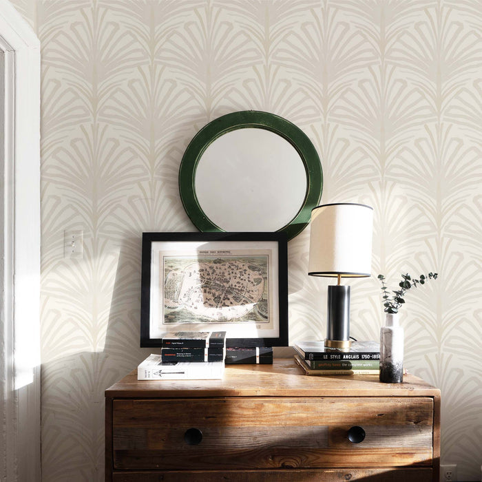 Suzy Sand wallpaper with subtle palm motif behind wooden dresser, styled with books, lamp, and round mirror, made-to-order USA