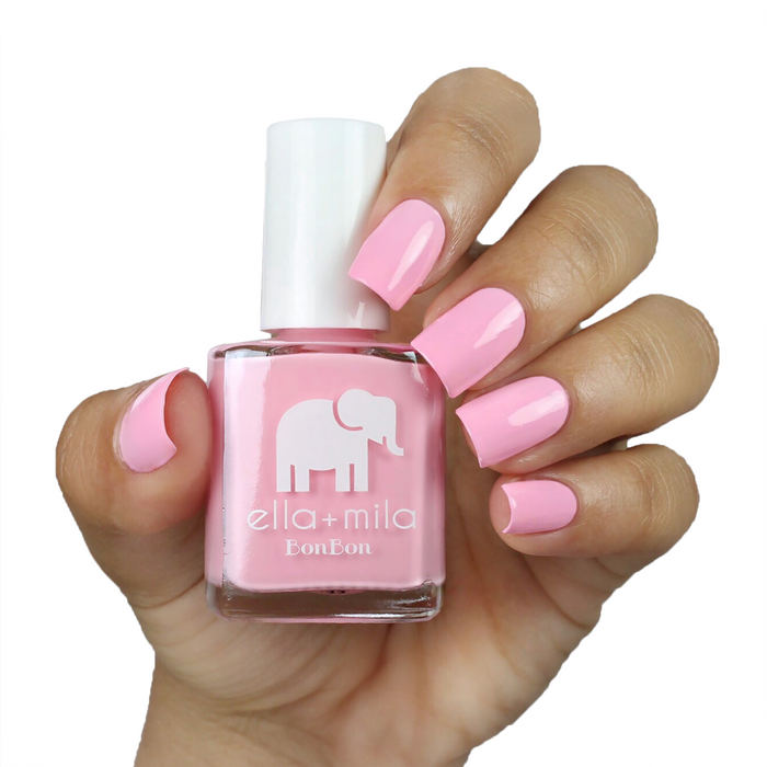 Team Sweets baby pink nail polish on a medium skin tone, hand holding the bottle