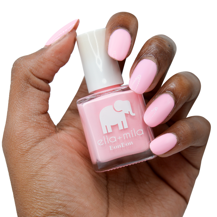 Team Sweets light baby pink nail polish on a deep skin tone, hand holding the bottle