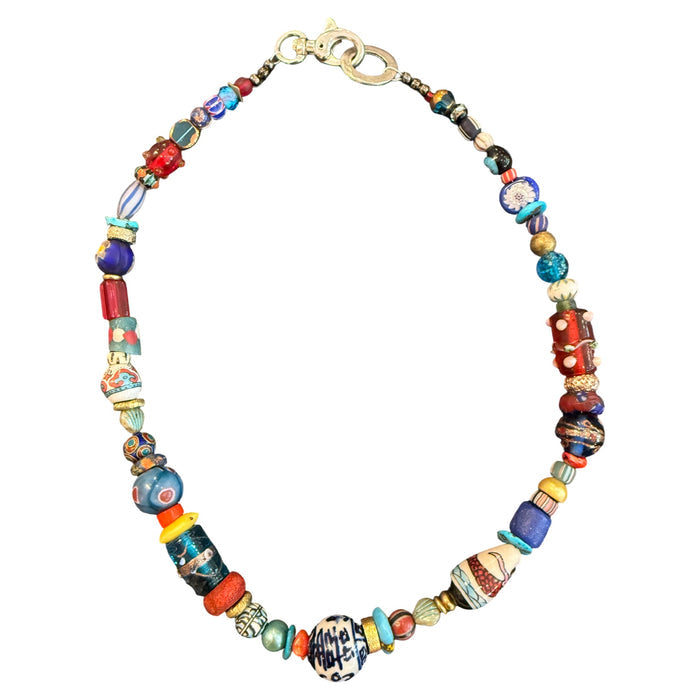 A handmade beaded necklace featuring a variety of colorful glass beads, including blue, red, yellow, and patterned designs, with a gold-tone clasp, shown on a plain white background.