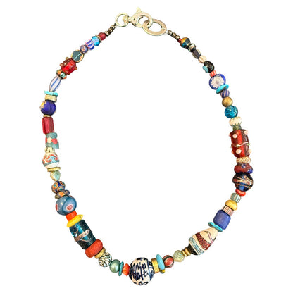 A handmade beaded necklace featuring a variety of colorful glass beads, including blue, red, yellow, and patterned designs, with a gold-tone clasp, shown on a plain white background.