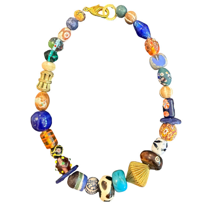 A multicolor beaded necklace with a gold clasp, featuring a variety of glass and ceramic beads in blue, orange, green, brown, and gold tones, displayed on a solid white background.