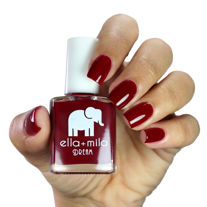 Wicked Red deep burgundy nail polish on a medium skin tone, hand holding the bottle
