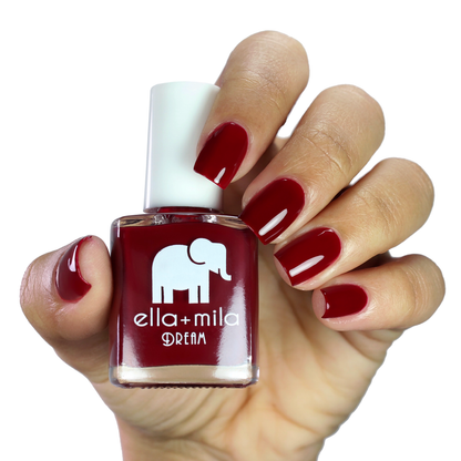 Wicked Red deep burgundy nail polish on a medium skin tone, hand holding the bottle