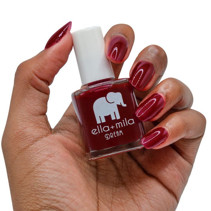 Wicked Red deep burgundy nail polish on a deep skin tone, hand holding the bottle