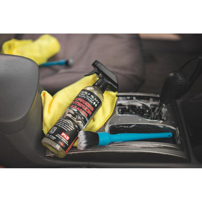 A spray bottle of P & S Xpress, Synthetic Detailing Brush, and yellow towel on the center console of a car.